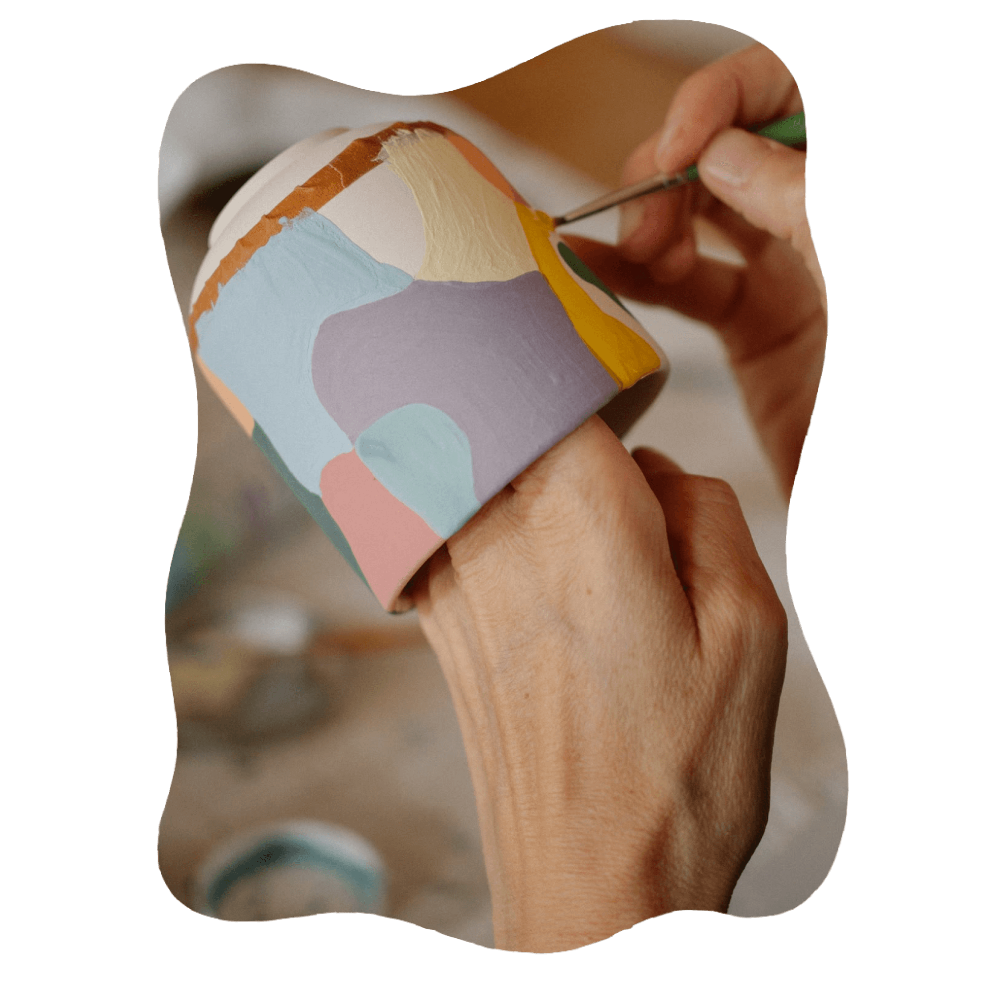 Two hands holding a small ceramic pot painted in blocks of soft blue, lilac, pink, yellow and green, a fine brush adding the last line.