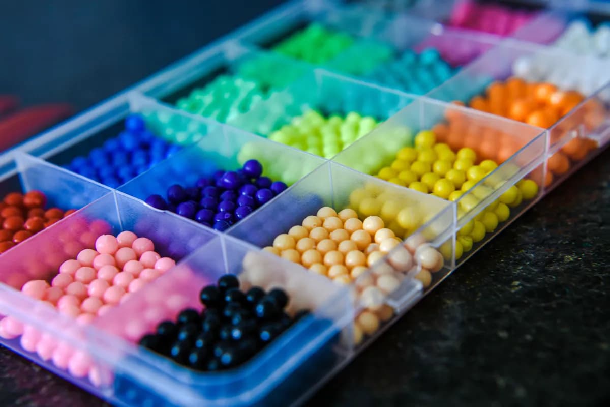 A sorting tray of beads laid out by colour — pink, blue, green, yellow, orange and black.