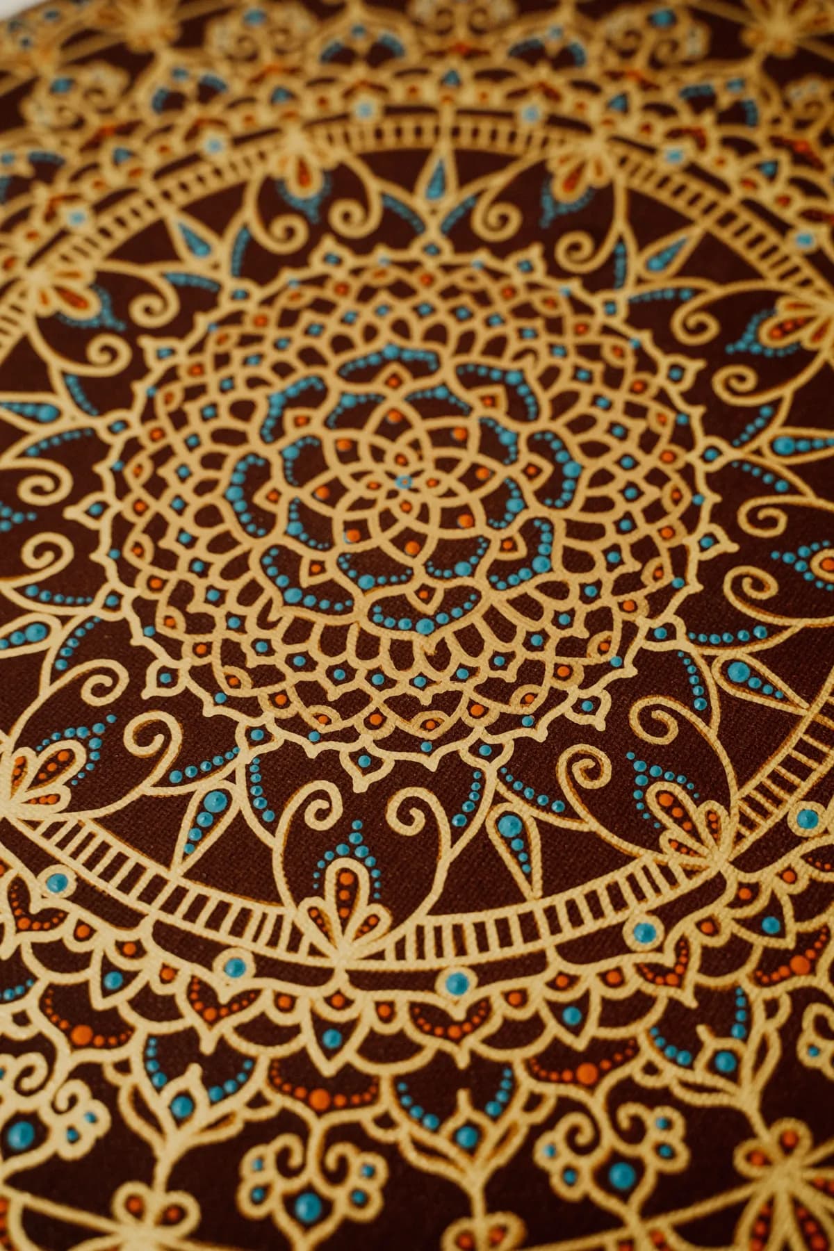 A mandala worked in gold line and turquoise dots across a deep brown ground, filling the frame.