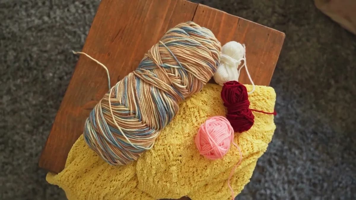 Balls of yarn in cream, red and a variegated blue resting on a finished mustard crochet piece.